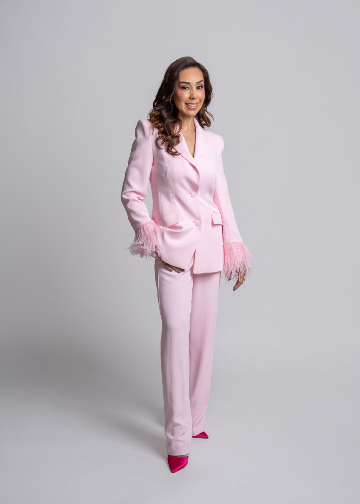 CONDUCTORA DE TELEVISION VESTIDO CON UN TRAJE EN COLOR ROSA EN FONDO BLANCO