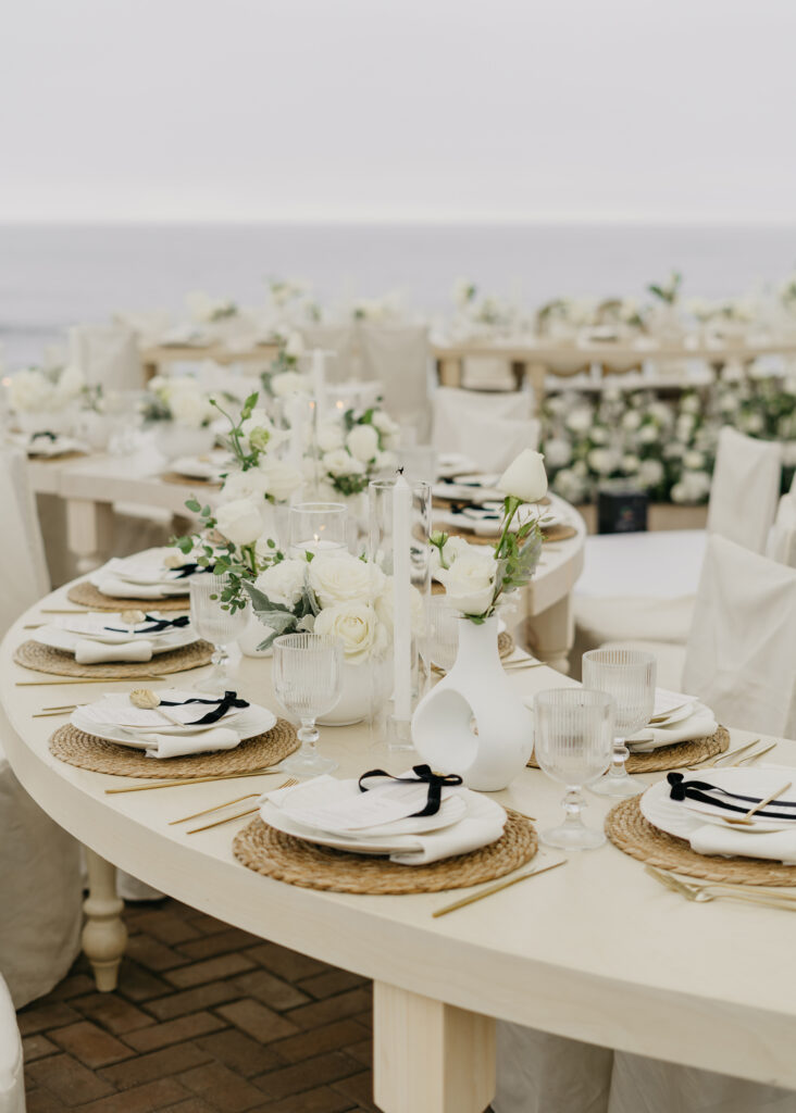 FOTOGRAFIA DEL MONTAJE EN DONDE SE VE LA DECORACION DE LA MESA, FLORES, COPAS, PLATO Y BAJO PLATO JUNTO CON EL MENU IMPRESO, CUCHARA, TENEDOR Y CUBIERTO
