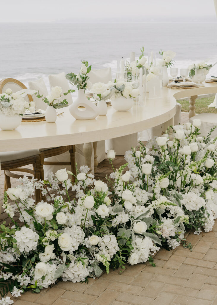 FOTOGRAFIA DEL MONTAJE EN DONDE SE VE LA DECORACION DE LA MESA, FLORES, COPAS, PLATO Y BAJO PLATO JUNTO CON EL MENU IMPRESO, CUCHARA, TENEDOR Y CUBIERTO